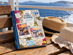 Family vacation photo album on a ferry bench with sun hats and the Aegean Sea behind