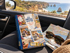 Adventure travel photo book on a car seat with sunglasses and a road map above the Algarve coast